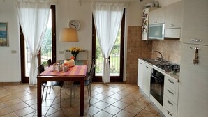 A kitchen with a dining area, featuring a table with chairs, a clock, a lamp, and a view of the outdoors.