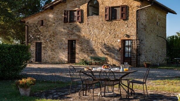 Un edificio de piedra con fachada rústica, un camino de entrada pavimentado y una mesa con sillas y un frutero.