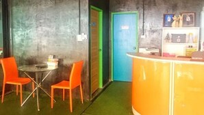 A room with a reception desk, two orange chairs, a green door, and a blue door. - T-House (Ratsada)