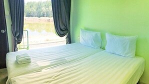 A neatly made bed with white linens and pillows, a folded towel on the side, and a view of a lake through the window. - T-House (Ratsada)