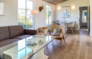 Una sala moderna con una mesa de centro de vidrio, un sofá marrón, sillas de mimbre y una zona de comedor con una mesa y sillas.