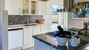 Een moderne keuken met witte kasten, een inbouwvaatwasser, een granieten aanrechtblad en een groot raam.