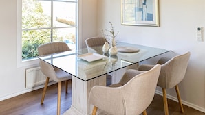 Een moderne eetruimte met een glazen tafel, vier stoelen en een vaas met takken.
