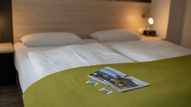 A hotel room with a neatly made bed, a green throw blanket, and a brochure on the bed. - Vacation apartment Grünstein, 1-2 persons, 30 sqm, upper floor (Schönau am Königssee)