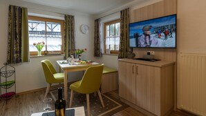 A dining area with a table, chairs, a television, and a window with curtains. - Vacation apartment Grünstein, 1-2 persons, 30 sqm, upper floor (Schönau am Königssee)