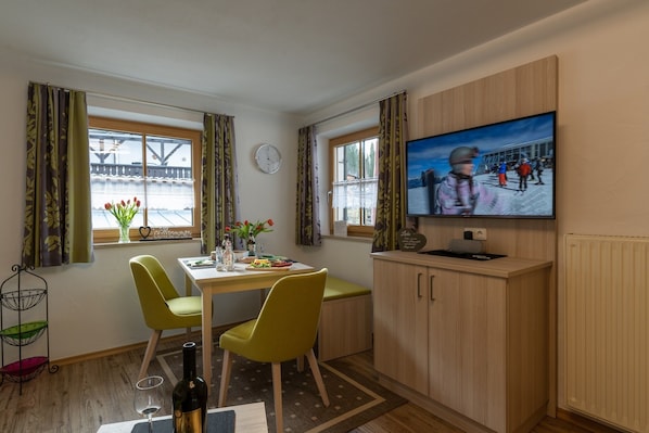 Un coin repas comprenant une table, des chaises, un téléviseur et une fenêtre avec des rideaux.