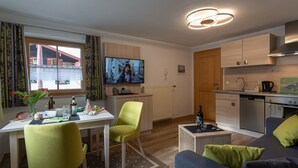 A modern kitchen with a built-in oven, a dining area with a table and chairs, and a living area with a sofa and a television. - Vacation apartment Grünstein, 1-2 persons, 30 sqm, upper floor (Schönau am Königssee)