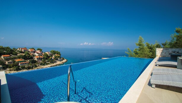 Uma piscina infinita azul límpida com vista para o mar e edifícios à beira-mar.