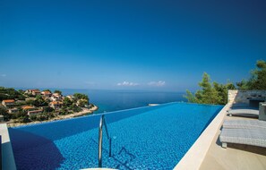 Una piscina infinita de color azul intenso con vista al mar y edificios costeros.
