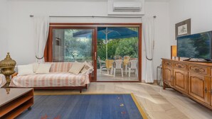 A living room with a sofa, a TV, a wooden cabinet, and a view of the outdoors through a glass door. - Lovely apartment in Njivice with house sea view (Njivice)