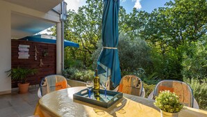 An outdoor patio with a table set for dining, surrounded by chairs, a potted plant, and a bottle of wine. - Lovely apartment in Njivice with house sea view (Njivice)