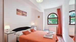 Een hotelkamer met een bed, nachtkastje, lamp, raam met gordijnen en een schilderij aan de muur.