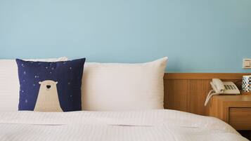 Una cama con almohadones blancos y azul marino, una mesita de noche de madera con un teléfono y una pared azul claro.