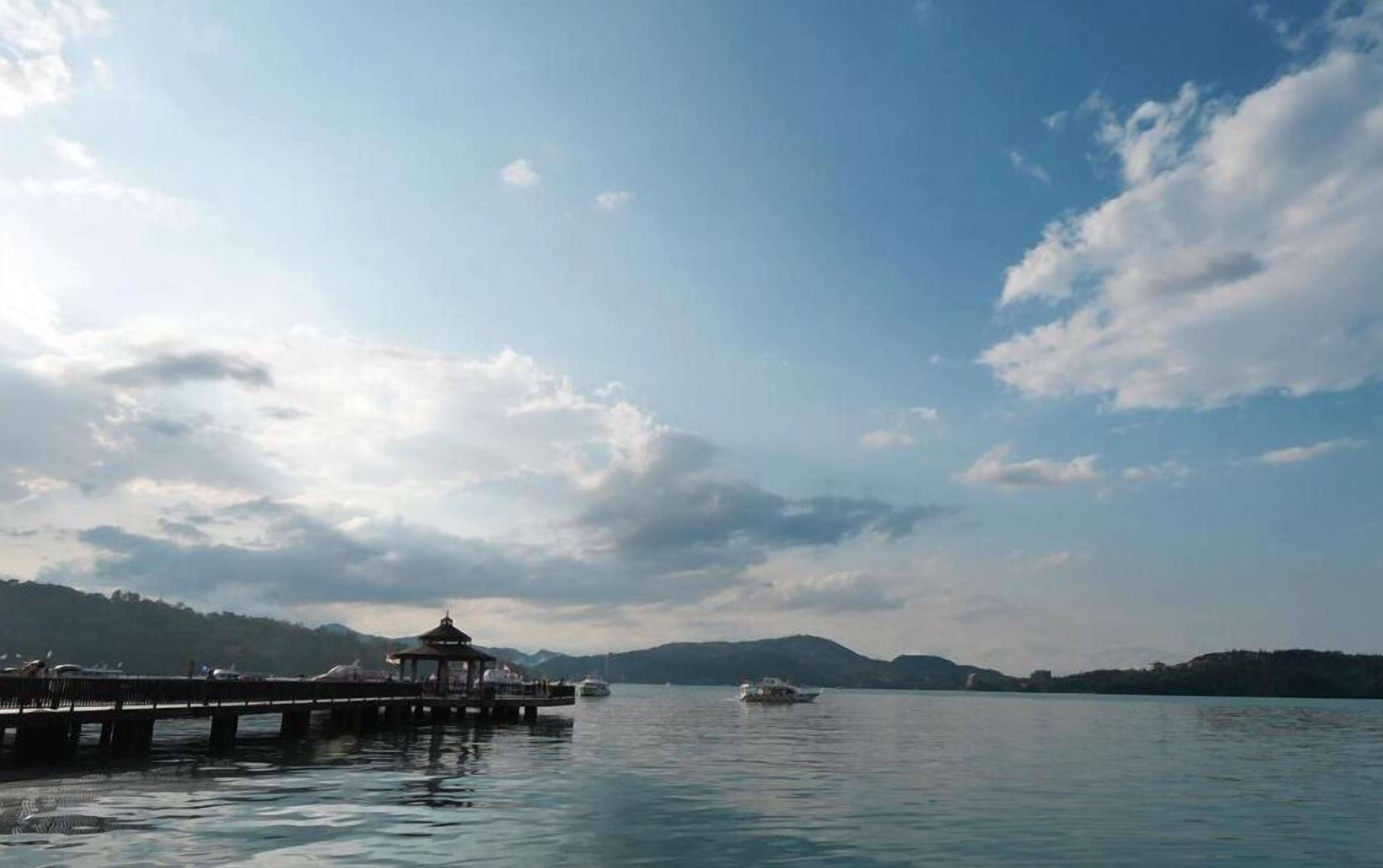 A calm lake with a pier and a gazebo. Boats are visible on the water.