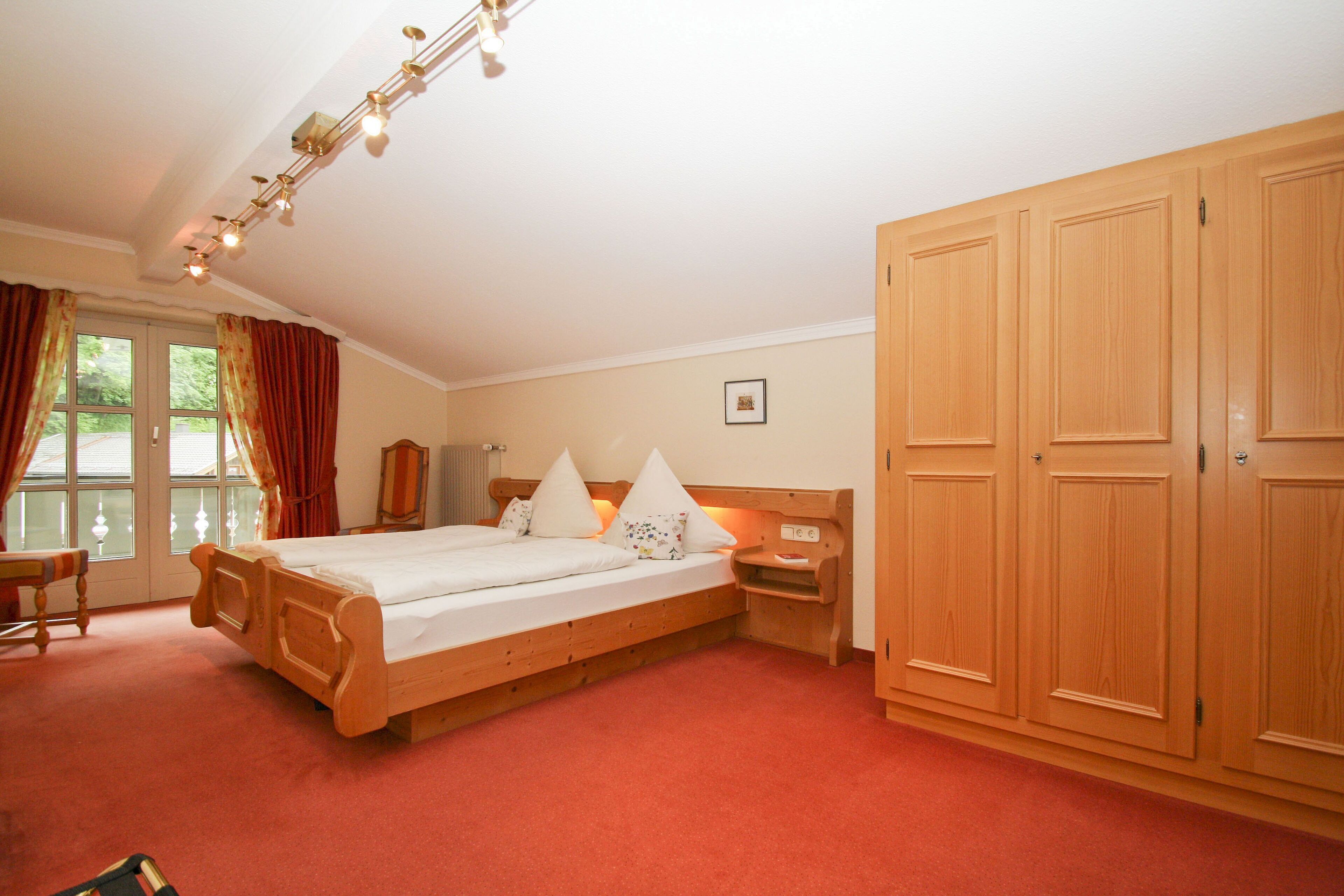 A bedroom with a wooden bed, a nightstand, a wardrobe, and a window with curtains.