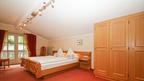 A bedroom with a wooden bed, a nightstand, a wardrobe, and a window with curtains. - Apartment 5, 77sqm, balcony, kitchen extra, 1 bedroom, 1 living room, 2 pers. (Ruhpolding)