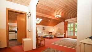 A spacious living area with a high ceiling, a dining table, a sofa, and a kitchen visible through an open door. - Apartment 5, 77sqm, balcony, kitchen extra, 1 bedroom, 1 living room, 2 pers. (Ruhpolding)