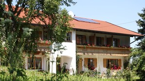 Un bâtiment à deux étages, doté d’un toit recouvert de tuiles rouges, de balcons ornés de jardinières et de panneaux solaires.