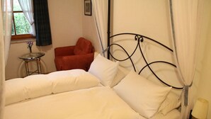 Un lit avec une literie blanche, une chaise rouge, une petite table ronde et une lampe de chevet.