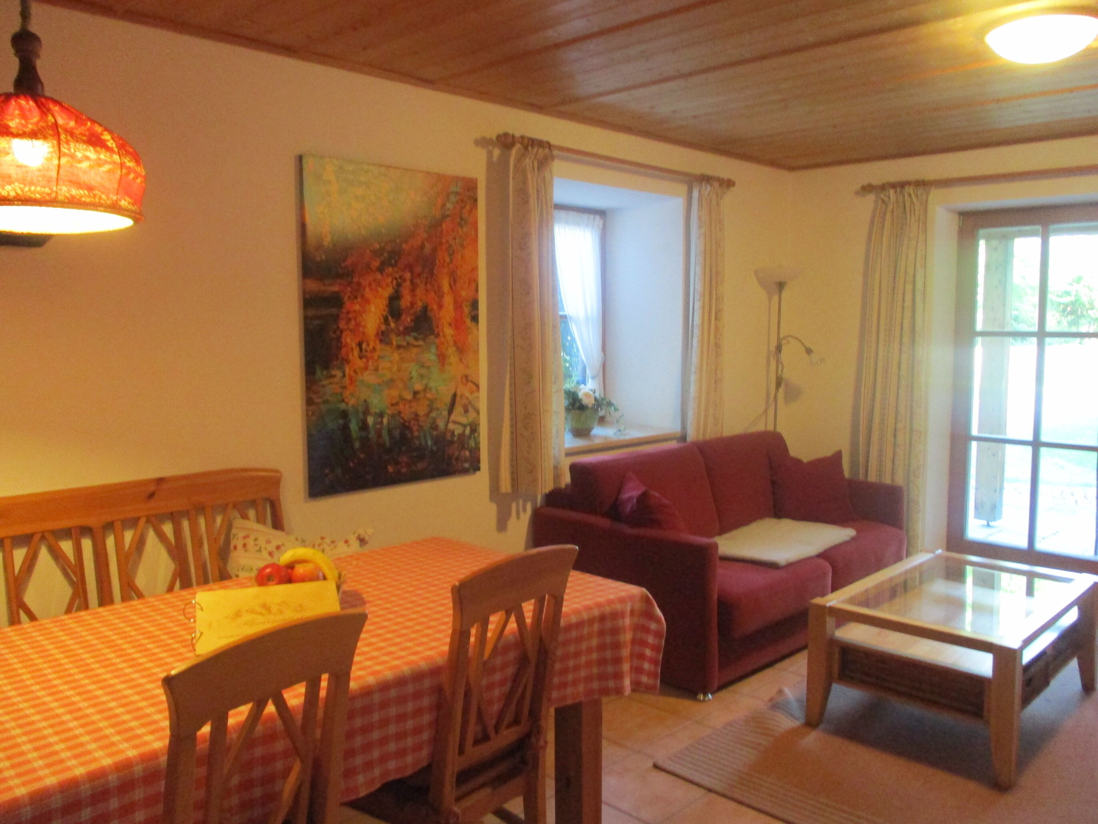 A room with a dining table, chairs, a sofa, a glass coffee table, and a painting on the wall.