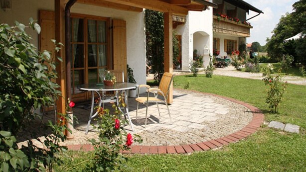 Une terrasse avec une table et des chaises, entourée d’une bordure en briques et d’une pelouse.