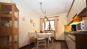 A compact kitchen with a dining table, chairs, a wooden cabinet, a microwave, and a window with curtains.