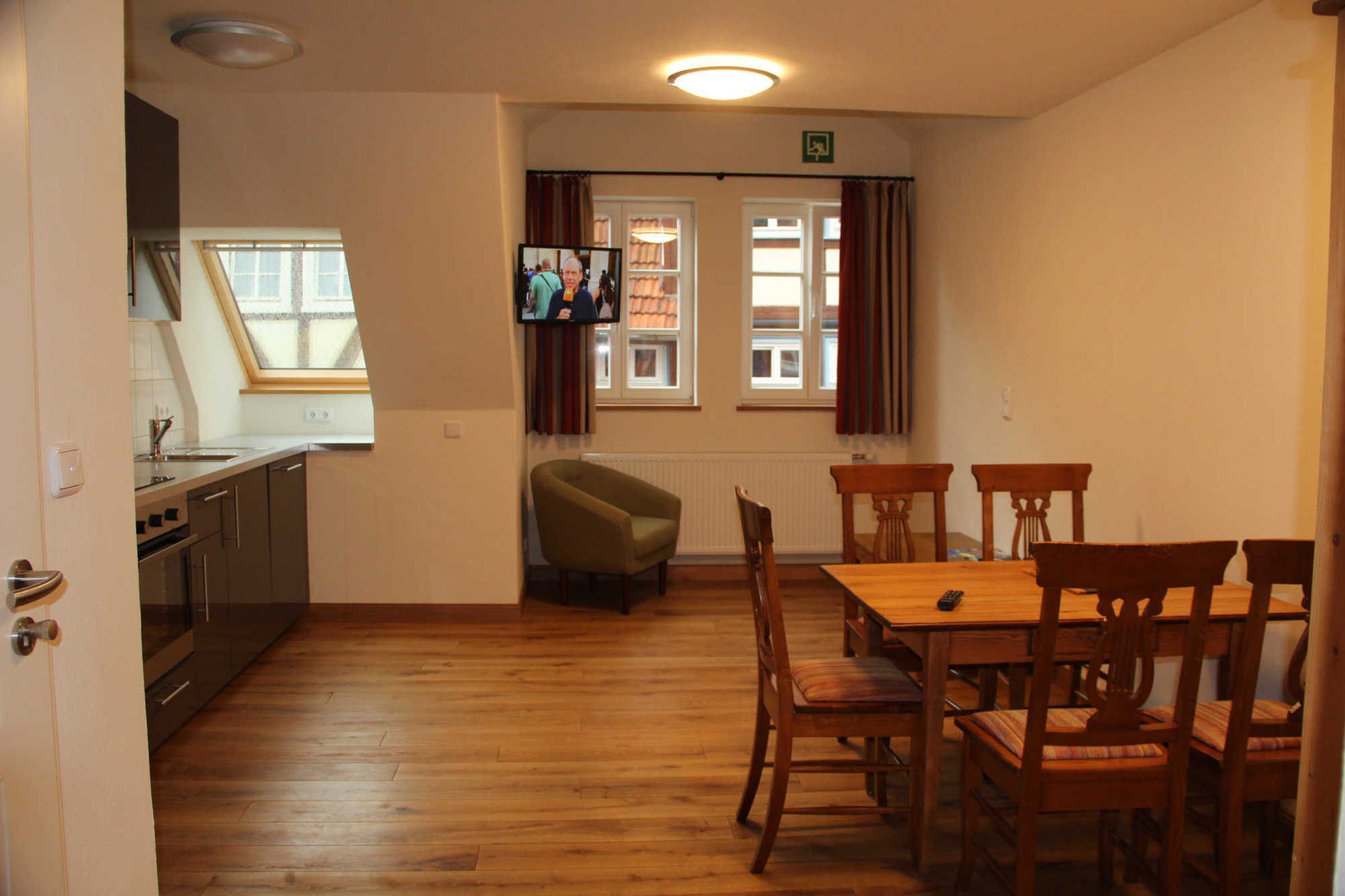 Ein Essbereich mit einem Holztisch und Stühlen, einem an der Wand montierten Fernseher und einem Fenster mit Vorhängen.