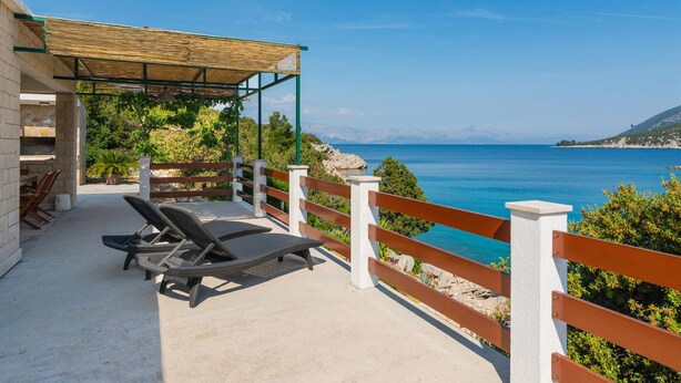 En balkong med två solstolar, en pergola och utsikt över havet.