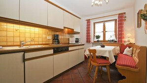 A kitchen with a sink, stove, and microwave. There is a dining table with a bench and a chair. - Apartment 2, 98sqm, balcony, kitchen, 2 bedrooms, 1 living room, max. 2 pers. (Ruhpolding)