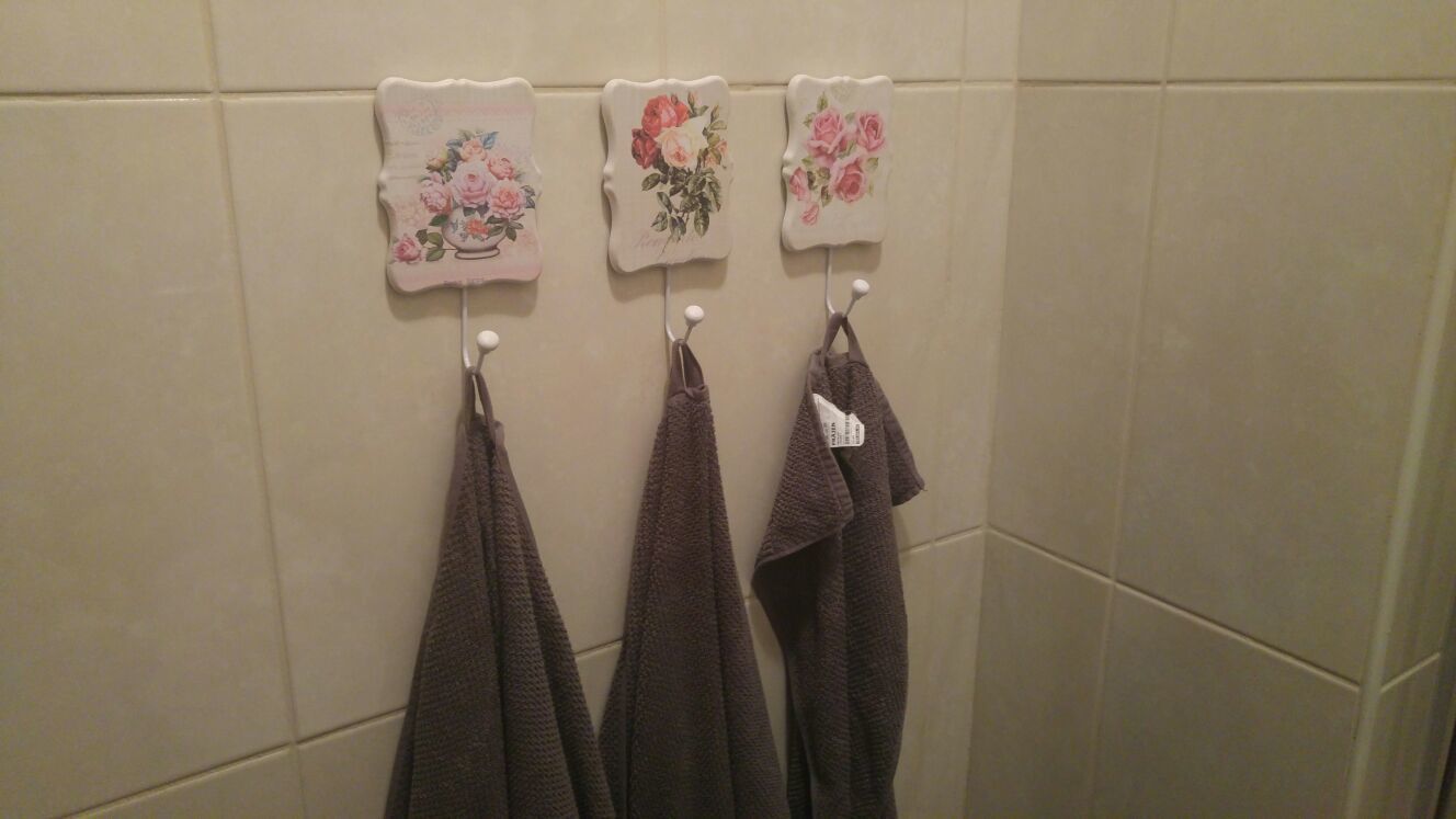 A bathroom with three towels hanging on hooks and three decorative wall tiles with floral designs.