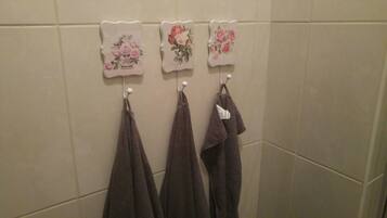 A bathroom with three towels hanging on hooks and three decorative wall tiles with floral designs.