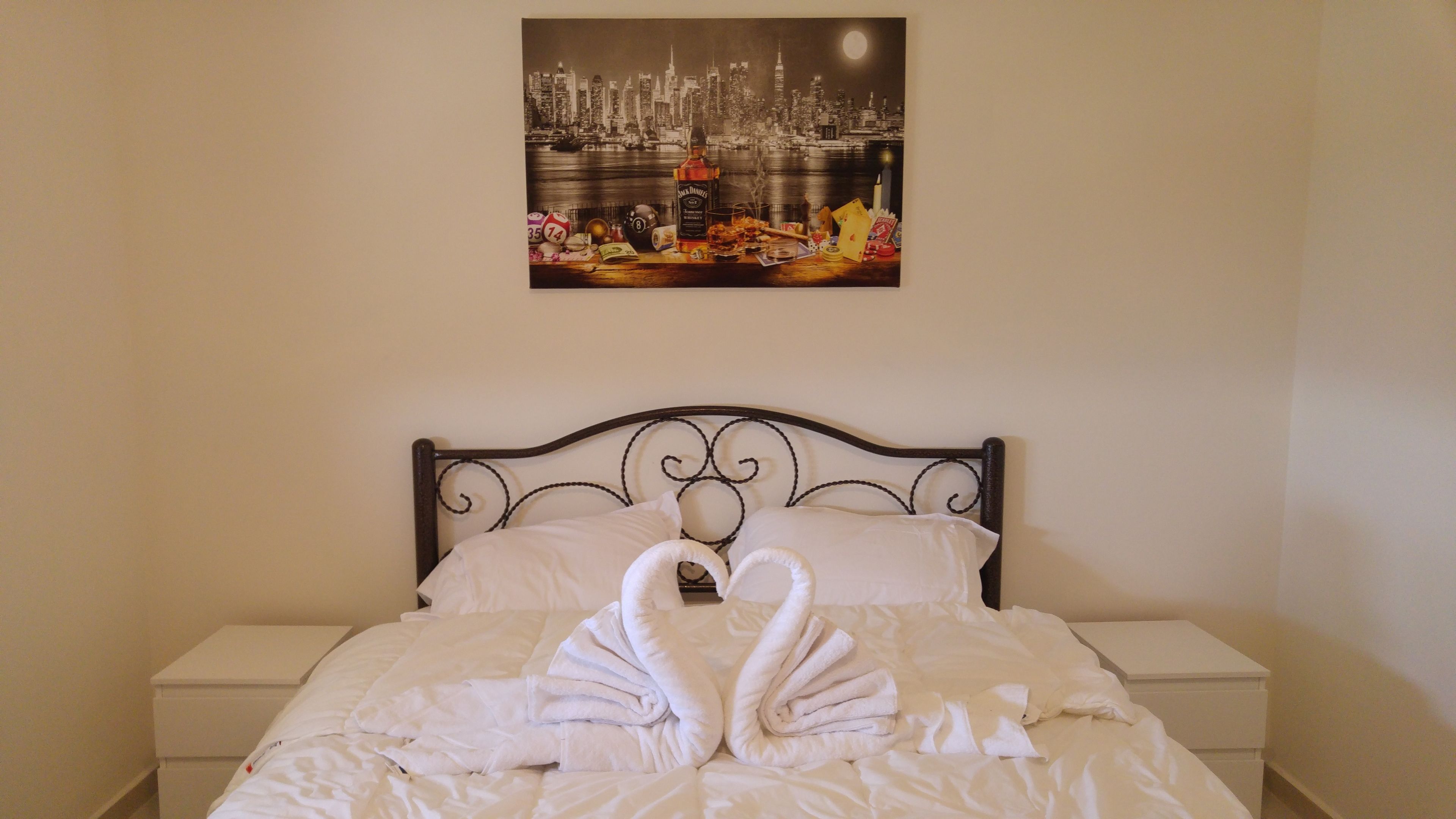 A bed with a swan-shaped towel arrangement, a cityscape painting above it, and a night sky.