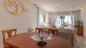 A hotel room with a dining table, chairs, a bed, a TV, and a view of the sea.