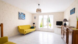 Een woonkamer met een gele bank, een televisie, een lamp en een kast.
