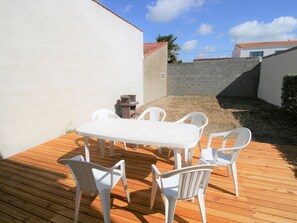 Een terras met een tafel en stoelen, een stenen muur en uitzicht op een gebouw met een rood dak.