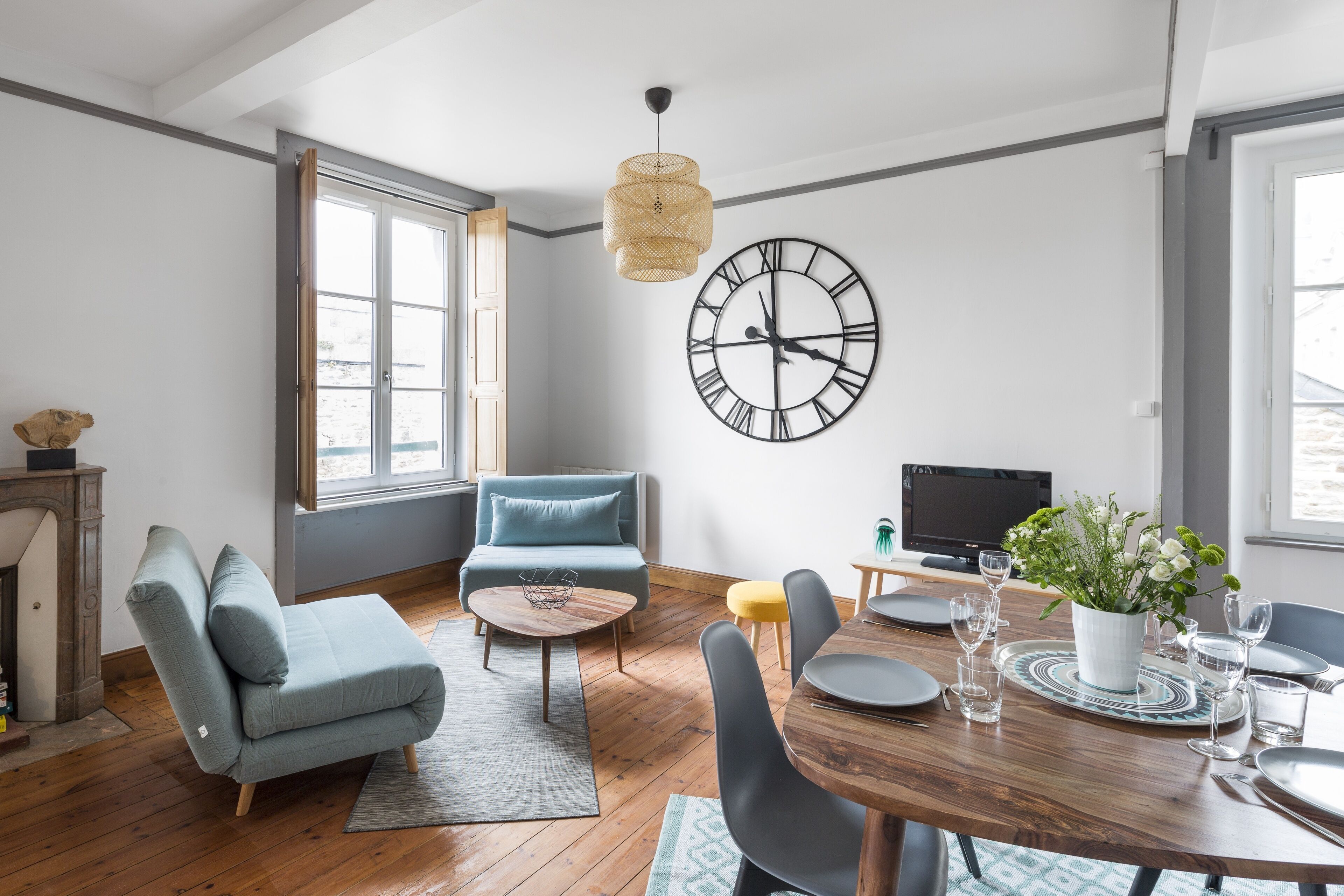 A modern living room with a sofa, coffee table, dining table set for four, and a large wall clock.