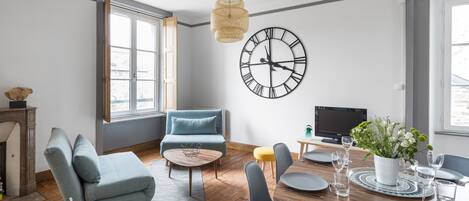 A modern living room with a sofa, coffee table, dining table set for four, and a large wall clock.