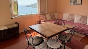 A cozy room with a dining table, chairs, a sofa with cushions, a window with a view of the sea, and a framed picture on the wall. - 3-room apartment 75m², 2 terraces, direct access to calanques, WIFI, private parking (Cavalaire-sur-Mer)