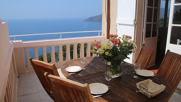 A wooden table set for two with a vase of flowers, a glass of water, and plates on a balcony overlooking the sea. - 3-room apartment 75m², 2 terraces, direct access to calanques, WIFI, private parking (Cavalaire-sur-Mer)