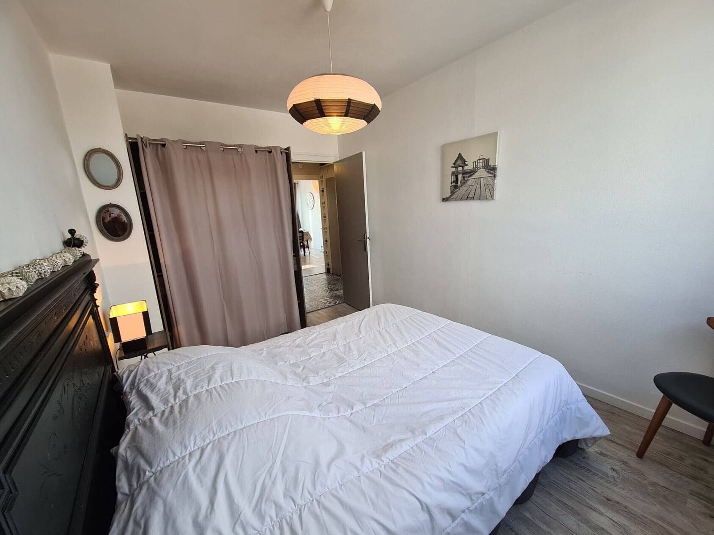 Een slaapkamer met een bed, een stoel, een nachtkastje met een lamp, een spiegel en een schilderij aan de muur.