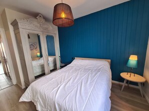 Une chambre avec un grand lit, un miroir, une commode et un mur bleu.
