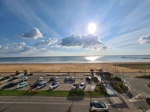 Un parking rempli de voitures, une plage et une jetée en arrière-plan.