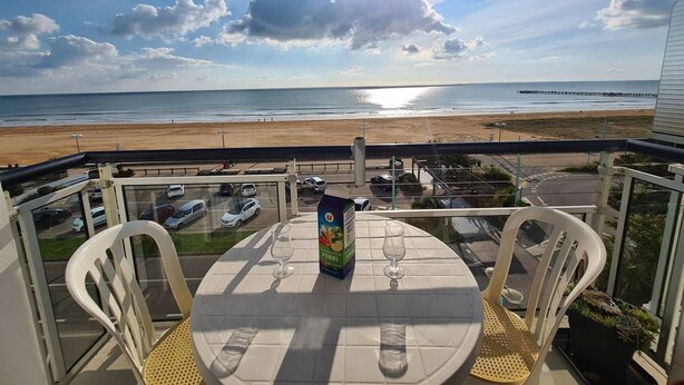 Een balkon met een tafel en stoelen, met uitzicht op het strand.