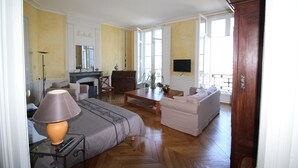 A living room with a sofa, armchair, and a television. There is a fireplace and a window with a view.