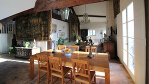 A spacious dining area with a wooden table and chairs, surrounded by large windows and a high ceiling with exposed beams.