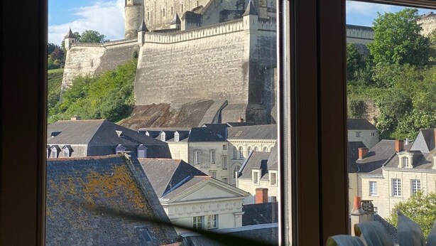 A view of a historic castle through a window, with a clear sky and surrounding buildings.