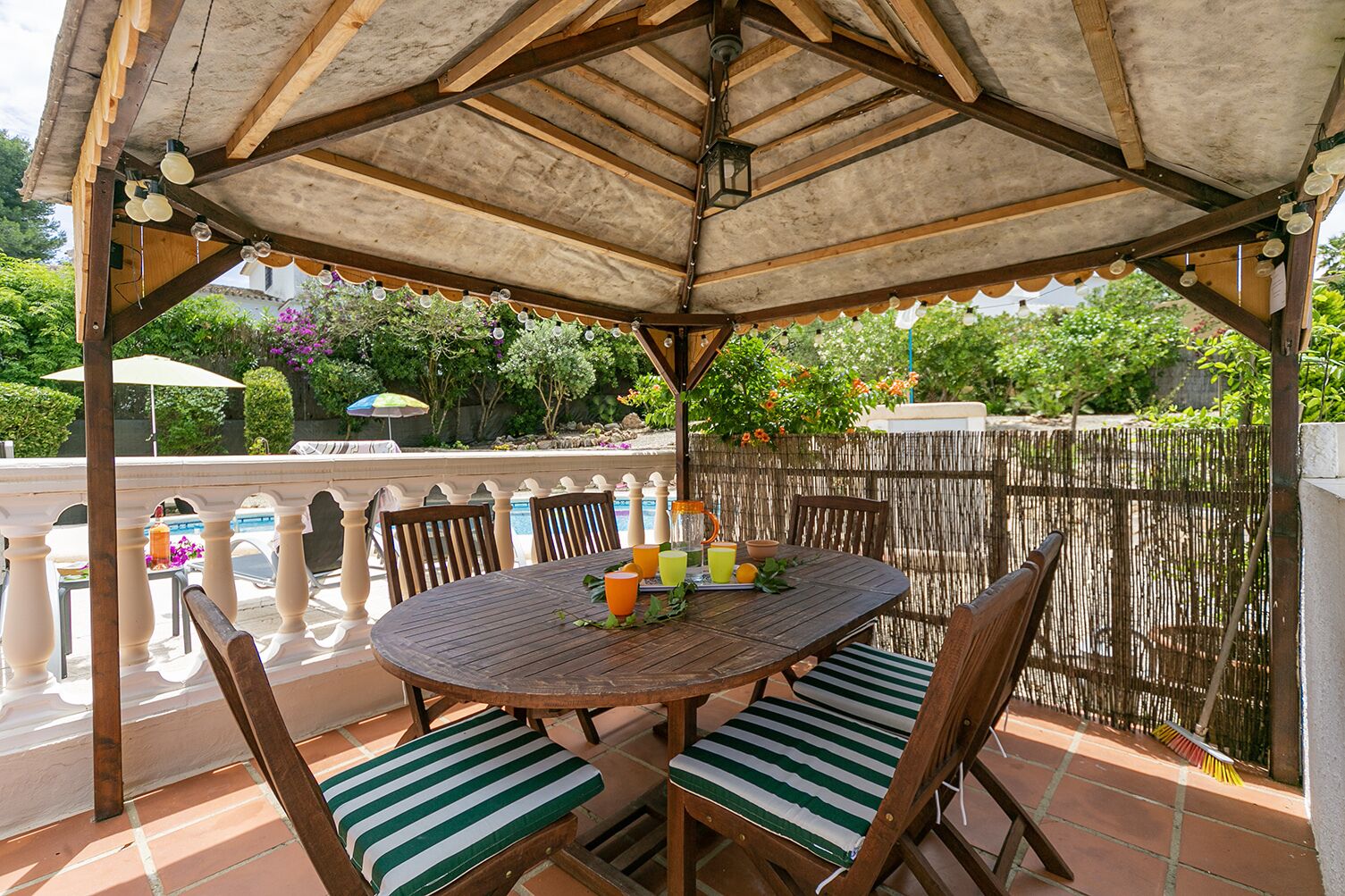 Une terrasse extérieure couverte, avec une table ronde en bois et des chaises à coussins à rayures.