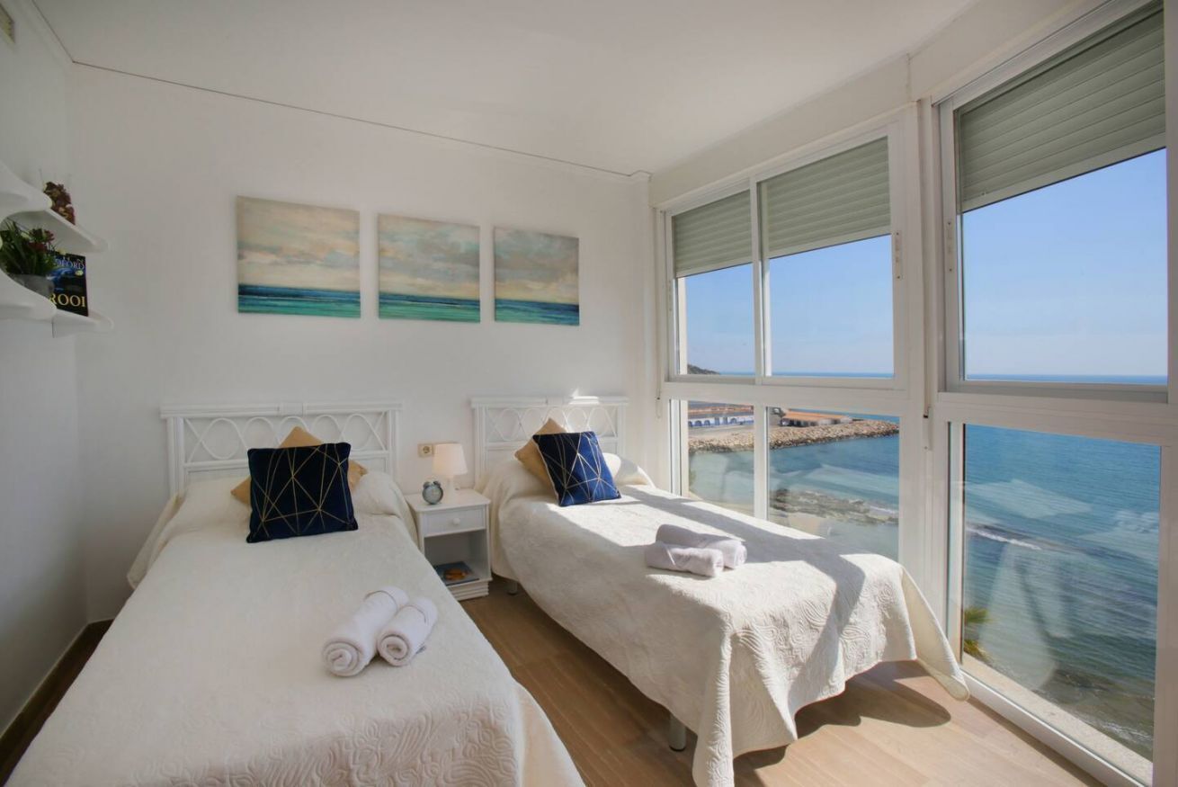 A hotel room with two beds, a large window with a view of the sea, and artwork on the wall.