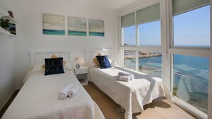 Une chambre d’hôtel avec deux lits, une grande fenêtre donnant sur la mer et des œuvres d’art accrochées au mur.