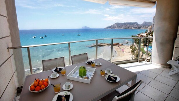 Un balcon avec une table préparée pour le petit-déjeuner, donnant sur une plage et la mer.